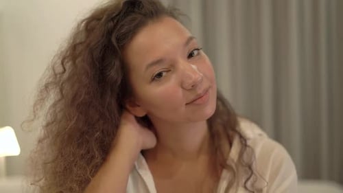 Joven somnolienta de raza mixta con camisa blanca arregla el cabello