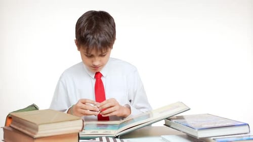 Young School Kid with Red Tie Sitting at Table with Books and Atlas Playing with Cube on White
