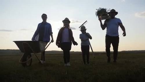 Young Family Having Fun Outdoors in Their Farm, Gardener Woman Pushing Wheelbarrow with Vegetables