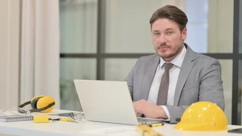 Middle Aged Engineer Smiling at Camera while using Laptop in Office