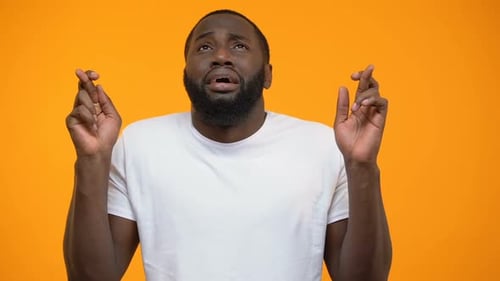 Superstitious African-American Man Crossing Finger and Praying for Good Luck