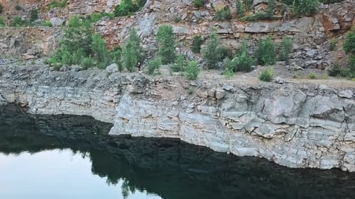Person Standing on Rocky Cliffside Above Calm Water