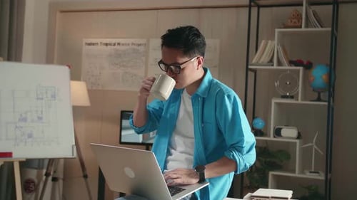 Man Engineer sitzt auf dem Tisch und trinkt Kaffee, während er einen Laptop benutzt, um im Büro zu arbeiten