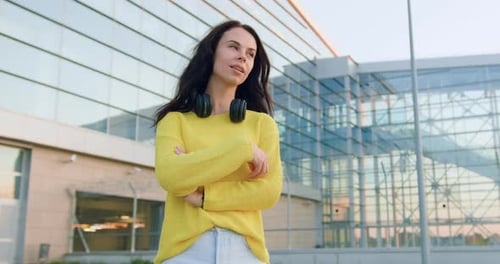 Mujer con ropa moderna que mira a la cámara con los brazos cruzados cerca de un gran edificio urbano moderno