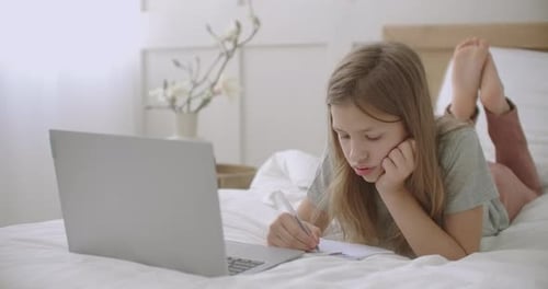 Bored Schoolgirl Is Drawing in Copybook During Online Lecturing of Teacher on Laptop, Homeschooling
