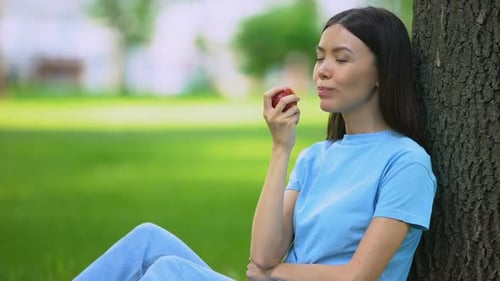 Woman Eating Apple While Leaning Against Tree