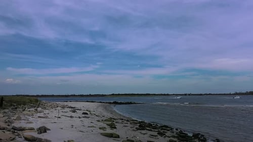 A low angle drone shot of an empty beach on a sunny day. The camera dolly out slowly over the rocky