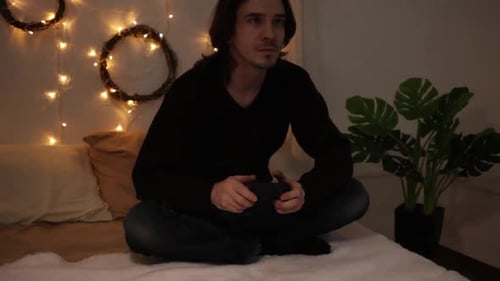 Young Adult Man Plays Video Game on Bed