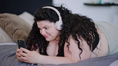 Woman Uses Smartphone on Bed Wearing Headphones