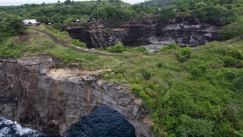 Aerial approaching broken beach showing archway with an incredible little cove on Nusa Penida. Indon