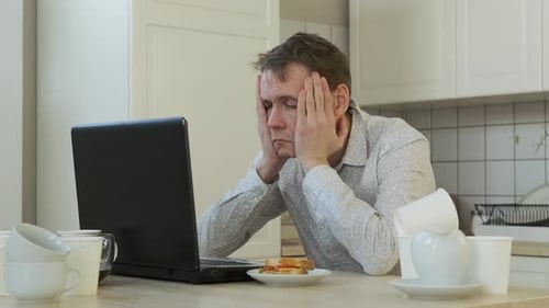 Tired Adult Working on Laptop in Kitchen