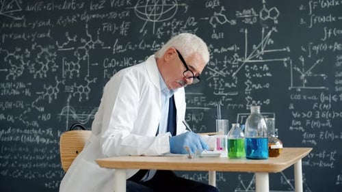 University Professor Writing in Class at Desk with Chemical Equipment Glass Tubes