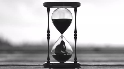 Sand running through the bulbs of retro hourglass on the head of depressed man.
