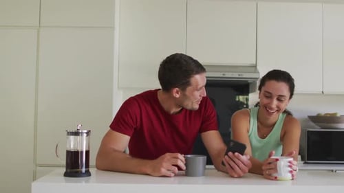 Happy caucasian couple drinking coffee and using smartphone