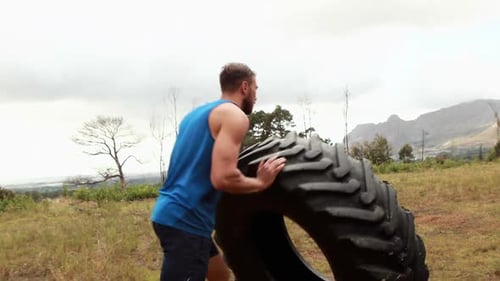 Homme en forme poussant un pneu lourd pendant une course d'obstacles