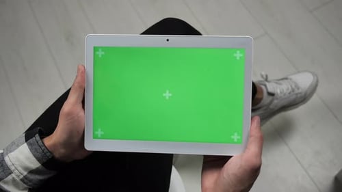 Mann sitzt auf Stuhl und blickt auf digitales Tablet mit Greenscreen-Chroma-Key