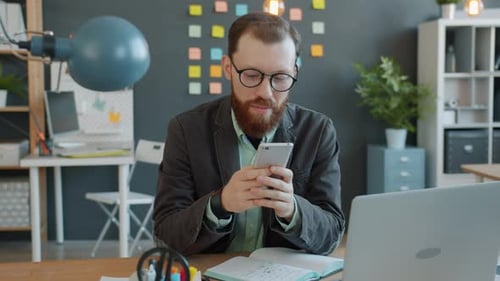 Handsome Businessman Using Smartphone in Office at Desk Enjoying Communication Online