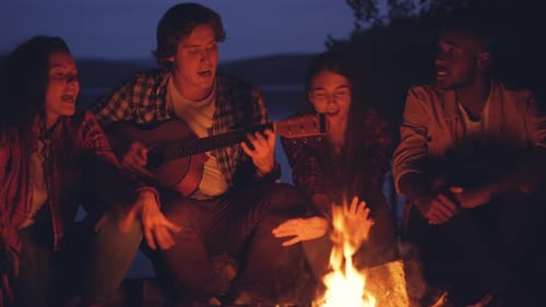 Friends Singing with Guitar Around Campfire at Night