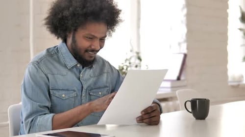 Excited Young Adult Reads a Document at Work
