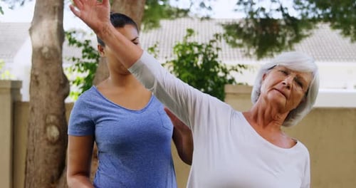 Young Woman Assists Senior Woman with Arm Stretch