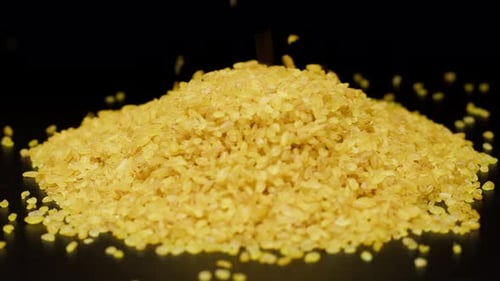 Pouring Yellow Bulgur in Pile on Dark Surface