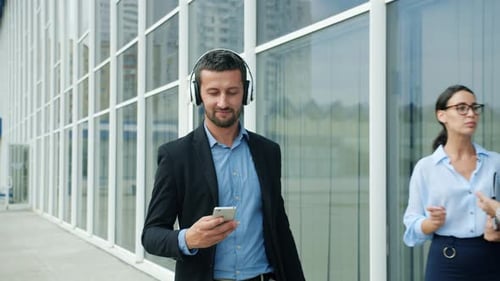 Man Walks with Headphones, Phone Outside Modern Building