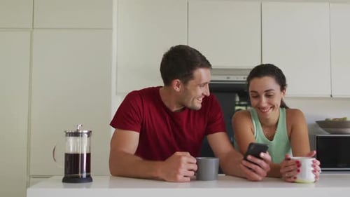 Couple Laughing Together Using Smartphone in Modern Kitchen