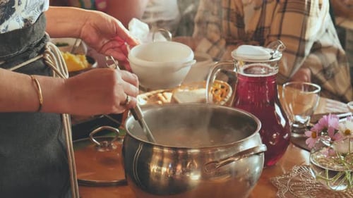 A Woman Pours Hot Soup for Guests