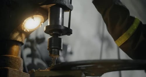 Metallarbeiter in Sicherheit Uniform bohrt Stahldetail auf einer vertikalen Bohrmaschine in der Werkstatt