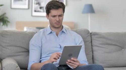 Man Uses Tablet While Sitting on Couch at Home