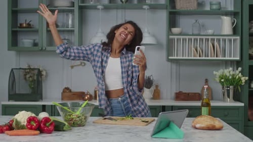 Enthusiastic Woman Dances in Kitchen with Smartphone