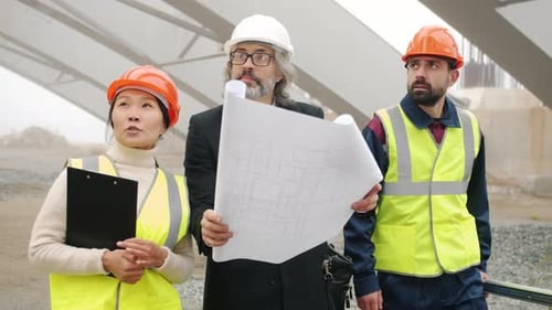 Architect Talking to Construction Workers Showing Blueprint Walking in Building Area Outdoors