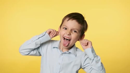 Lustiger kleiner Junge, der dumme Gesichter macht. Junge im blauen Hemd klebt an der Zunge in UHD