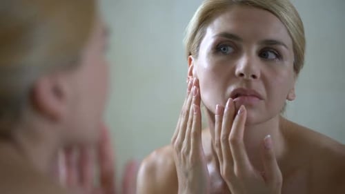 Woman Examining Her Face in Mirror with Concern
