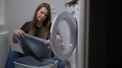 Woman Loading Gray Towels into Washing Machine