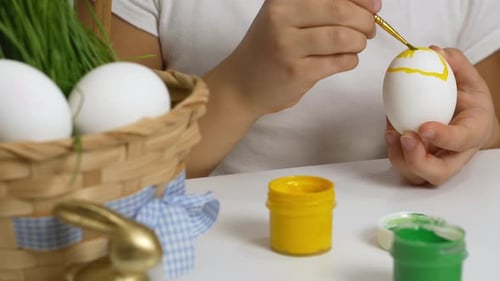 Children drawing on painted eggs at the table, at home. Preparing for the Easter holiday.
