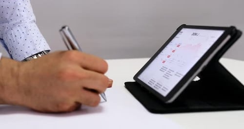 Adult Analyzing Data on Tablet and Taking Notes