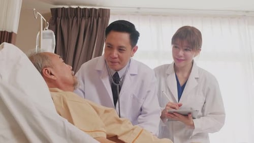 Asian professional doctor and nurse taking care of elderly male patient lying down on bed.