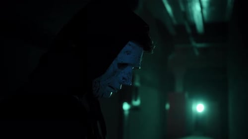 Eerie Figure in Mask and Hooded Cloak in Dark