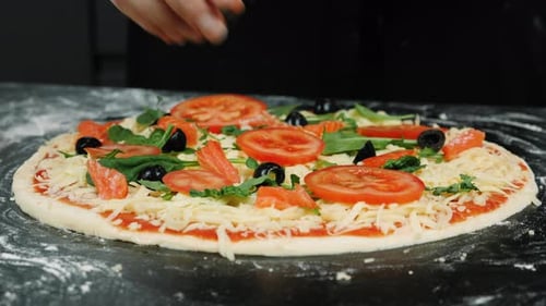 Weibliche Hände verteilen Zutaten auf Pizzateig und kochen zu Hause traditionelle italienische Pizza