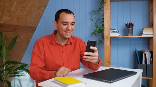 Smiling Man Video Chats on Smartphone at Desk