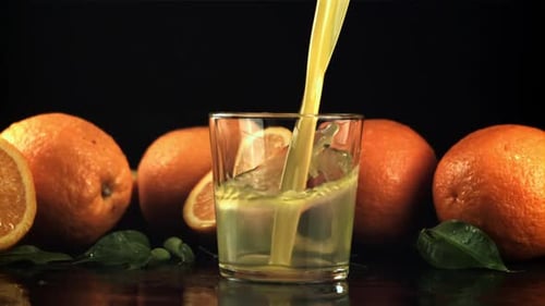 A Stream of Orange Juice with Splashes Pours Into the Glass