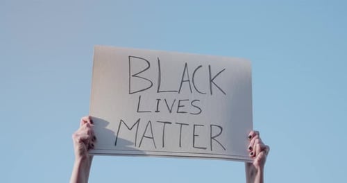 Arms Holding Black Lives Matter Sign Against Blue Sky