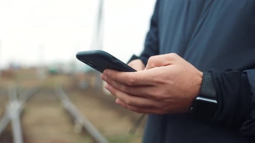 Man Using Smartphone Outdoors near Train Tracks
