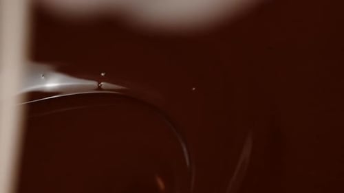 Un bâtonnet en bois fait remuer le chocolat noir fondu brillant avec des tourbillons et des tourbillons