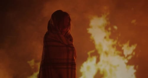 Mysterious Figure Stands Before Raging Fire at Night