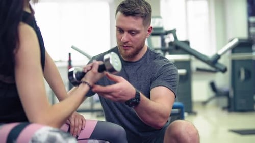 Man Instructing Woman Using Dumbbell at Gym
