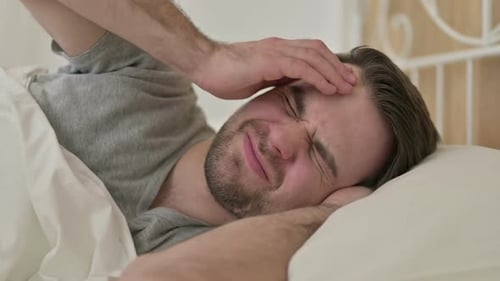 Porträt eines jungen Bartmannes mit Kopfschmerzen im Bett