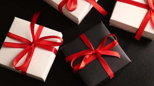Hand Places Black Gift Box Among White Gifts