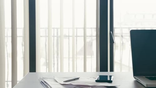 Modern Laptop on a Desk in an Office Next To Big Windows